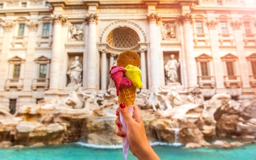 Włoskie lody rzemieślnicze w rożku trzymane na tle monumentalnej Fontanny di Trevi w Rzymie