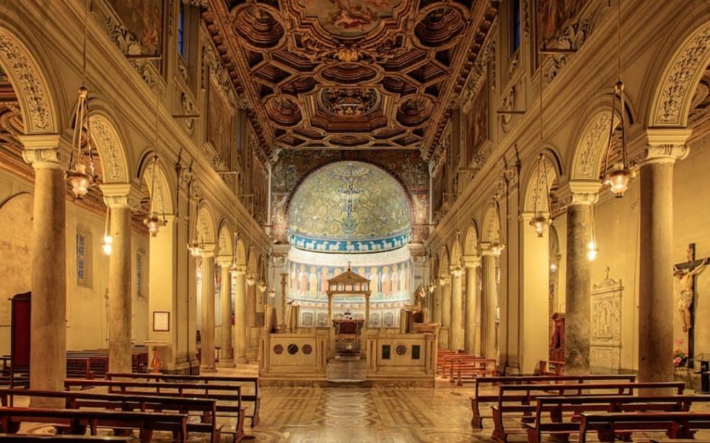 Wnętrze Bazyliki św. Klemensa w Rzymie ze złotą mozaiką i rzędami ławek przy ciepłym oświetleniu 