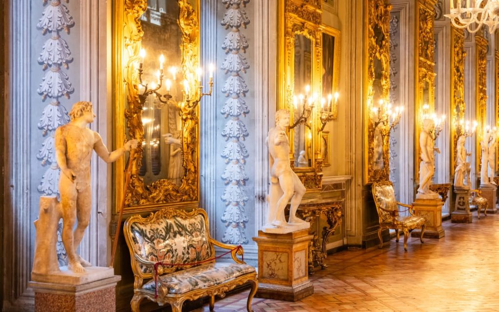 Wnętrze Galerii Zwierciadeł (Galleria degli Specchi) w Palazzo Doria Pamphilj w Rzymie ze złotymi kandelabrami i antycznymi rzeźbami