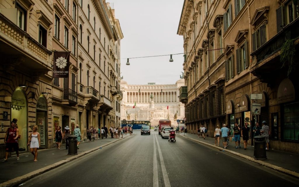 Zabytkowa ulica Via del Corso w Rzymie z ruchem ulicznym i monumentalnym pomnikiem w tle