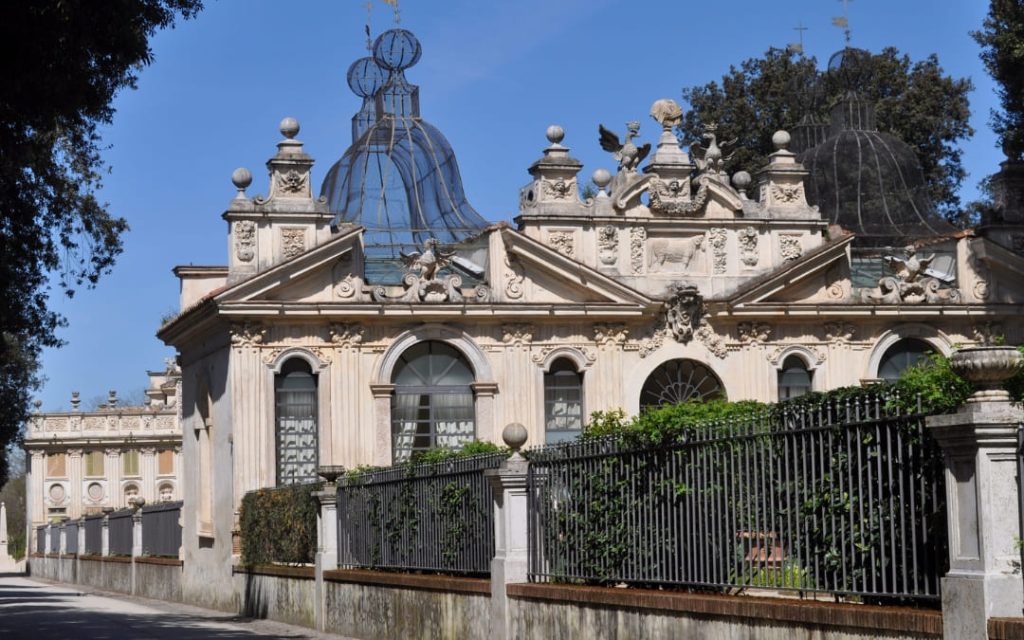 Zabytkowy budynek ptaszniki (Uccelliera) w ogrodach Villa Borghese w Rzymie z charakterystycznymi metalowymi kopułami na tle błękitnego nieba