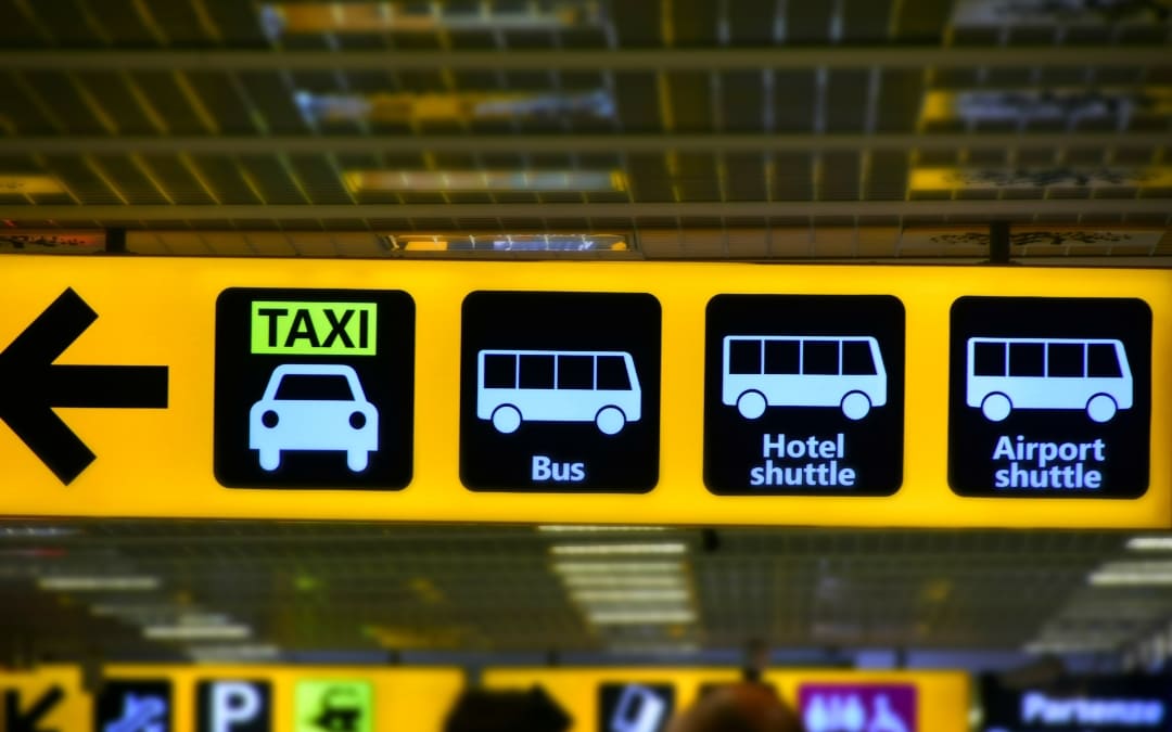 Żółta podświetlana tablica informacyjna na lotnisku z piktogramami i strzałką kierującą do taxi, autobusu i shuttle busa