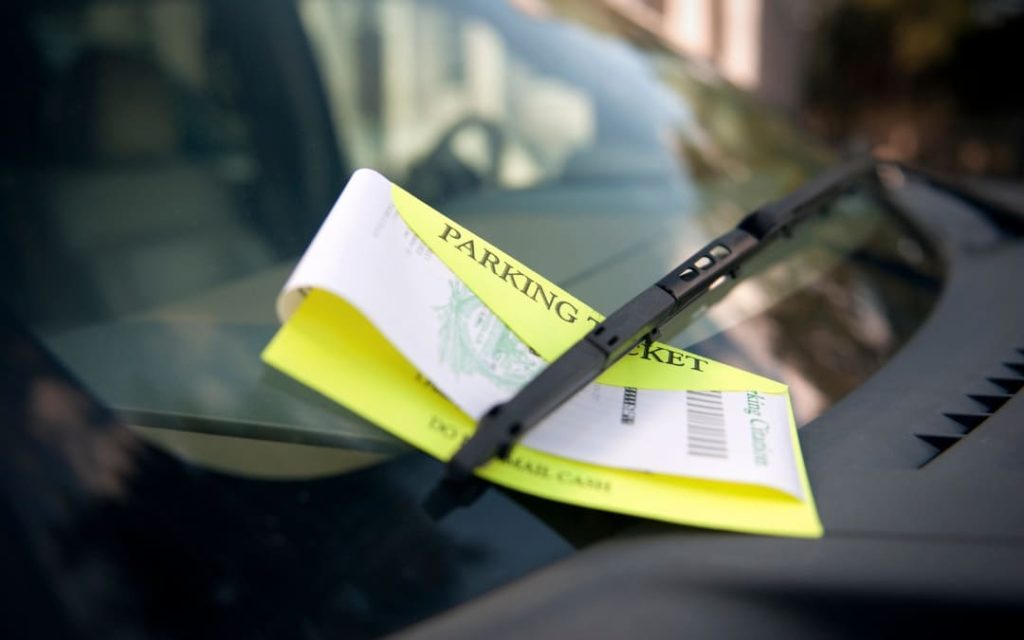 Żółty mandat za wycieraczką samochodu na przedniej szybie auta zaparkowanego na ulicy