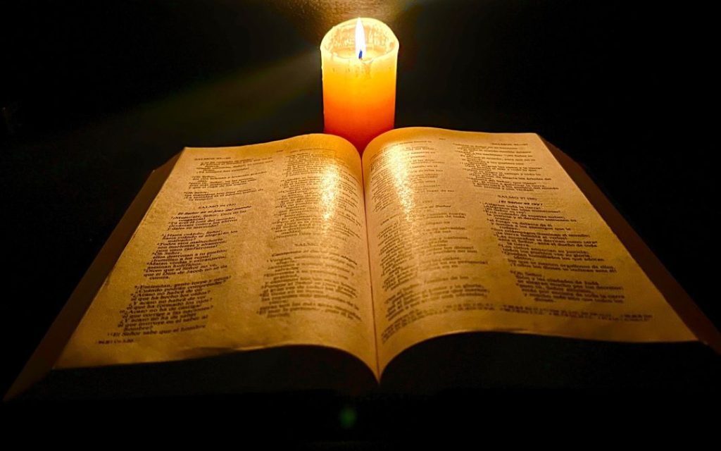 Biblia leżąca na stole z zapaloną świeczką