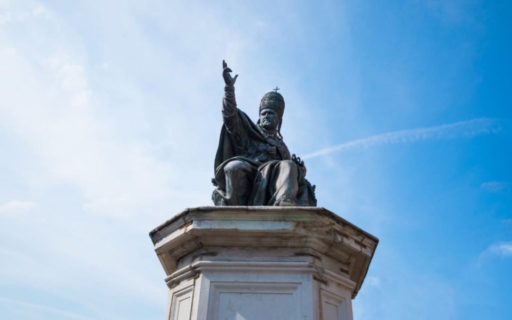 Brązowy pomnik papieża Pawła V z uniesioną ręką w geście błogosławieństwa na tle błękitnego nieba w Watykanie