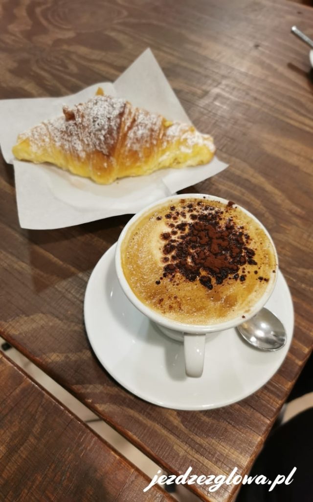Cappuccino z kakao i rogalik z cukrem pudrem na drewnianym stoliku w rzymskiej kawiarni