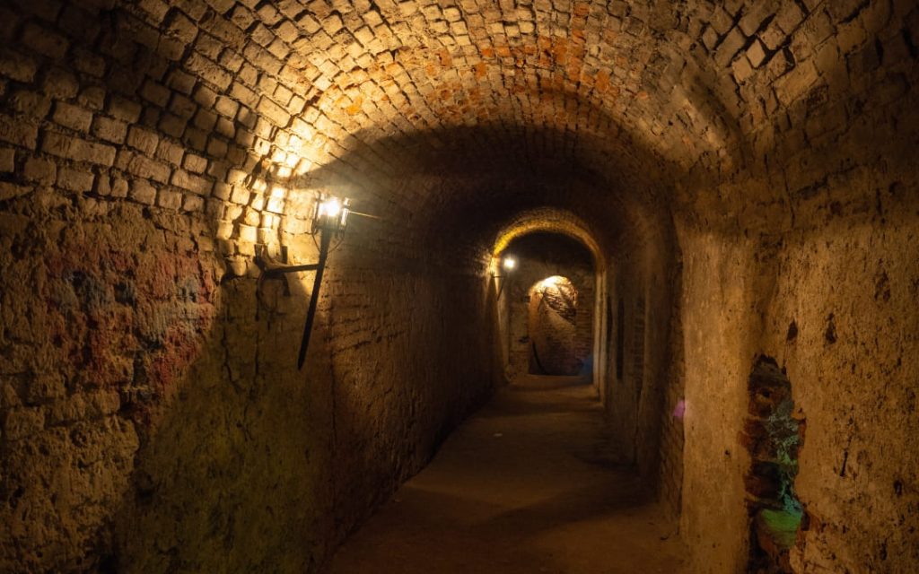 Długi ceglany tunel podziemny oświetlony ciepłymi lampami na ścianach
