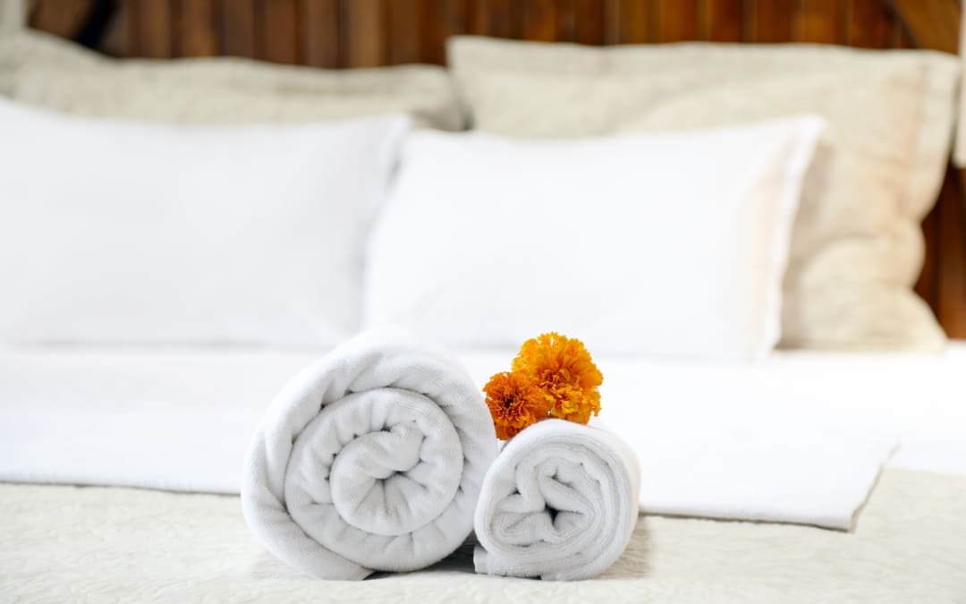 Dwa zwinięte białe ręczniki z pomarańczowym kwiatem na pościeli w pokoju hotelowym