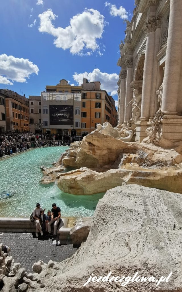 Fontanna di Trevi w Rzymie z turkusową wodą i grupą turystów siedzących przy basenie