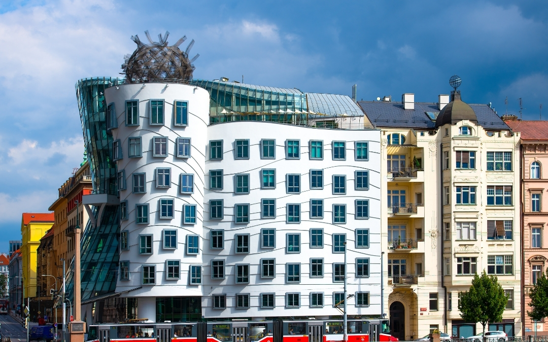 Frontalna panorama Tańczącego Domu w Pradze z metalową kopułą na dachu i tramwajem w tle