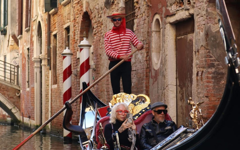 Gondolier w kolorowym stroju i charakterystycznym kapeluszem z czerwoną wstążką, prowadzący gondolę z turystami na pokładzie