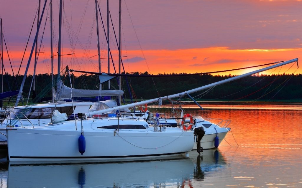 Jacht żaglowy zacumowany na spokojnym jeziorze mazurskim podczas spektakularnego, pomarańczowego zachodu słońca.