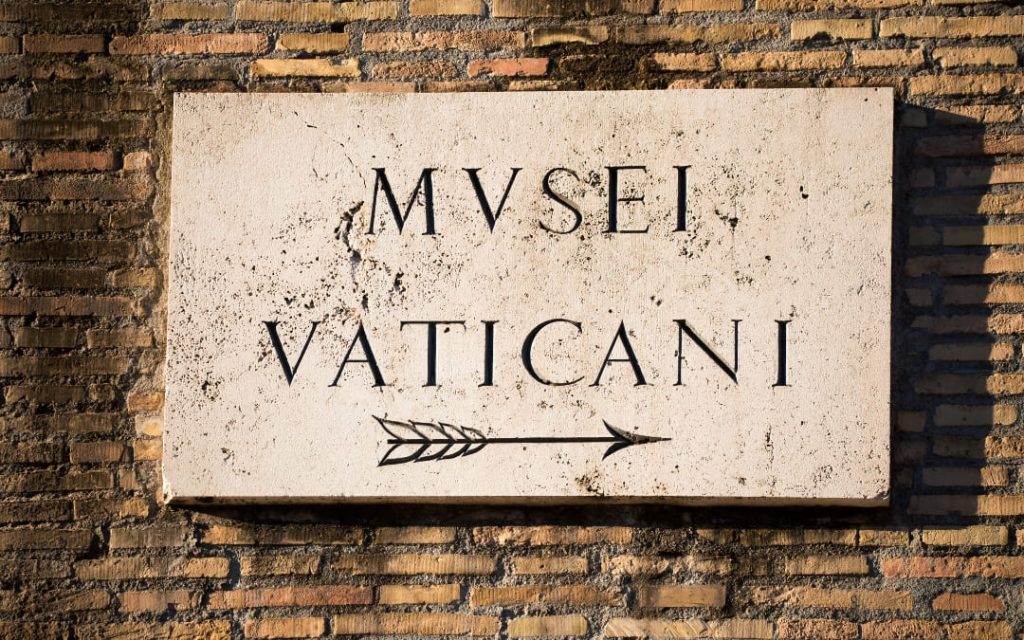 Kamienna tablica z napisem Musei Vaticani i strzałką wskazującą drogę do wejścia do Muzeów Watykańskich