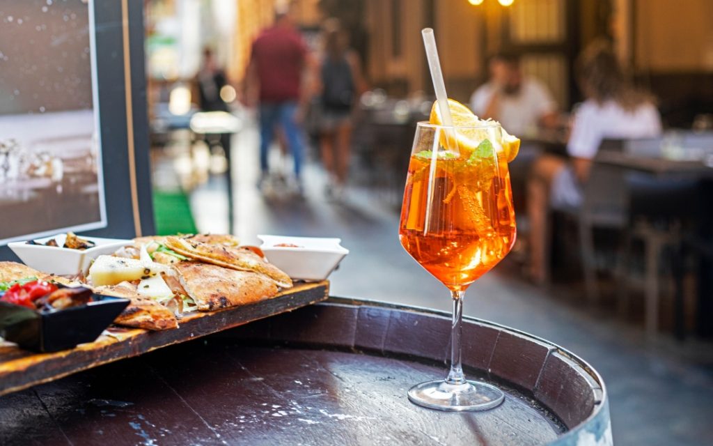 Kieliszek Aperol Spritz z pomarańczą na beczce przy talerzu z przekąskami w restauracji