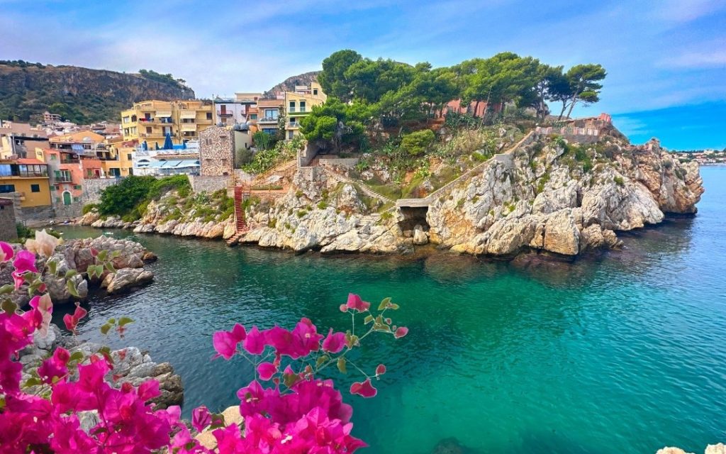 Kolorowe zabudowania miasteczka na skalistym zboczu nad turkusowym Morzem Jońskim na Sycylii.