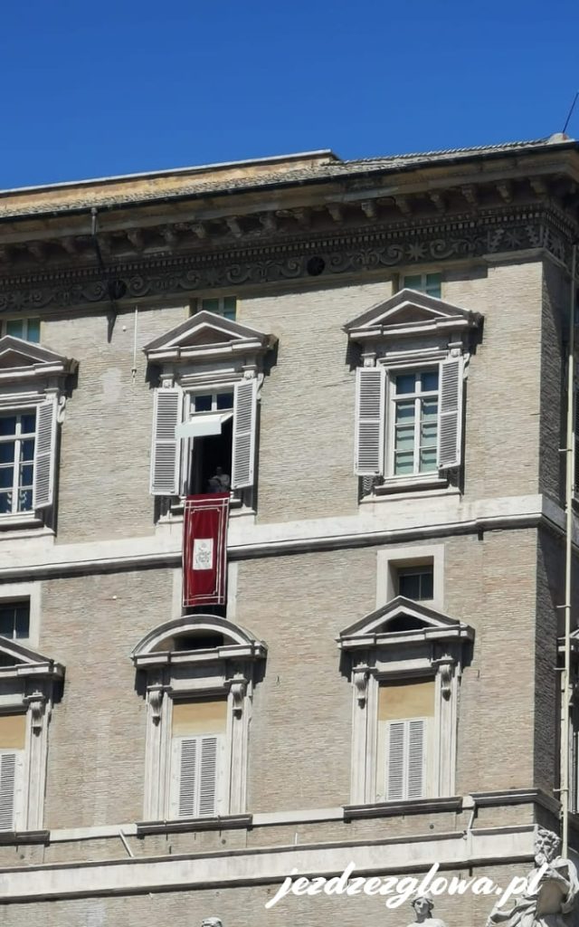 Okno papieskie z czerwonym herbem w fasadzie Pałacu Apostolskiego na Placu Świętego Piotra