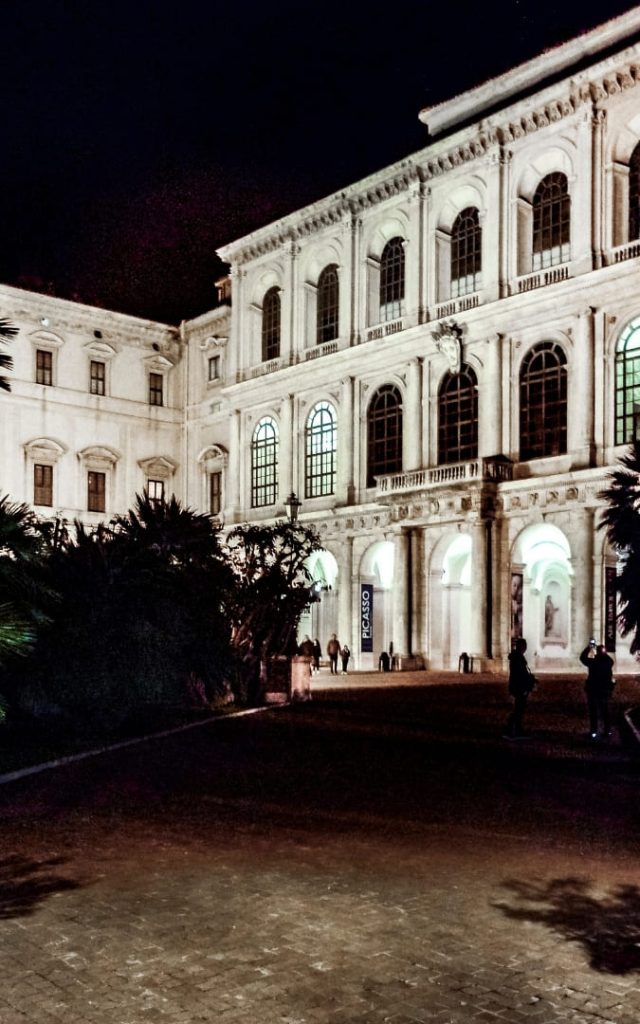 Palazzo Barberini w Rzymie oświetlone nocnymi reflektorami z przechodniami przy wejściu