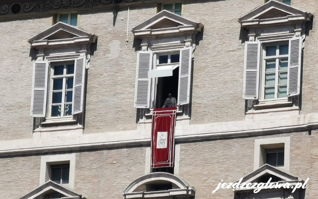 Papież Franciszek pojawiający się w oknie Pałacu Apostolskiego z czerwonym baldachimem na Placu Świętego Piotra