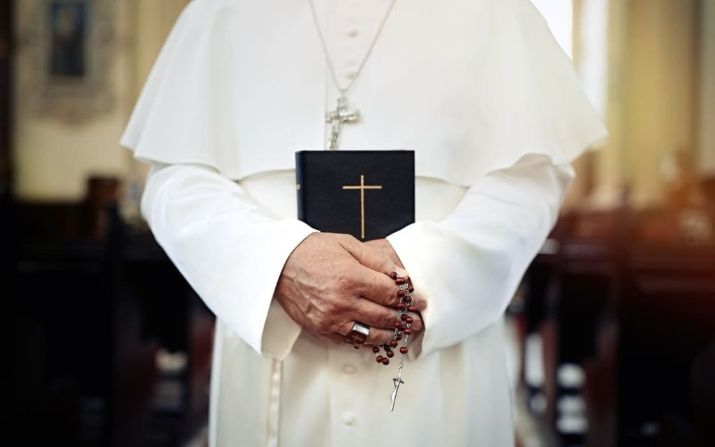 Papież w białej sutannie trzymający czarną Biblię ze złotym krzyżem oraz różaniec