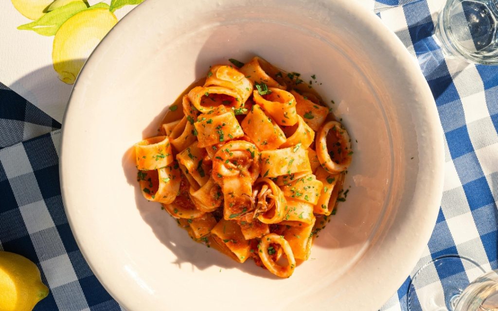 Pappardelle w sosie pomidorowym z kałamarnicą i pietruszką na białym talerzu w kratkę