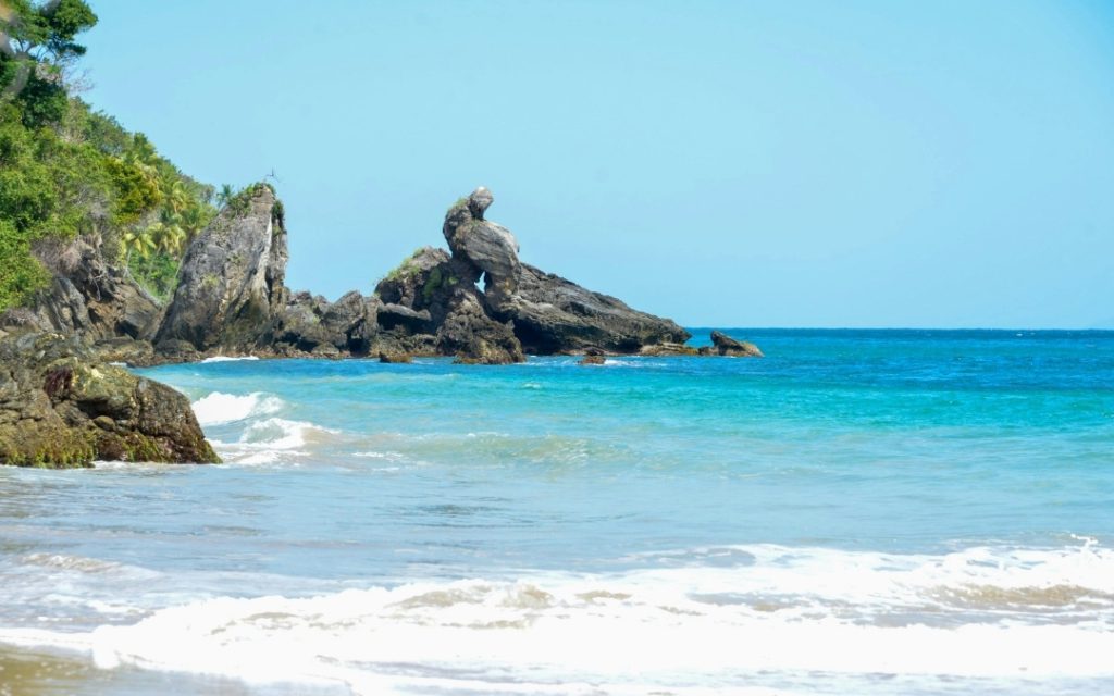 Piaszczysta plaża na Dominikanie z turkusową wodą i charakterystycznymi formacjami skalnymi.