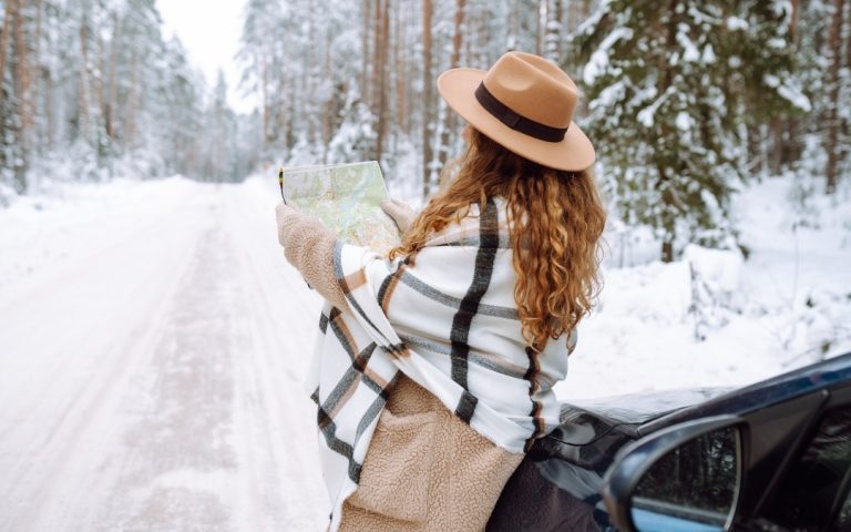 Podróżnik w zimowej odzieży analizujący mapę papierową na tle ośnieżonego lasu.