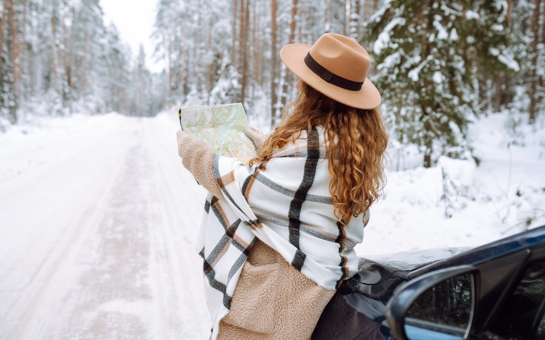Podróżnik w zimowej odzieży analizujący mapę papierową na tle ośnieżonego lasu.