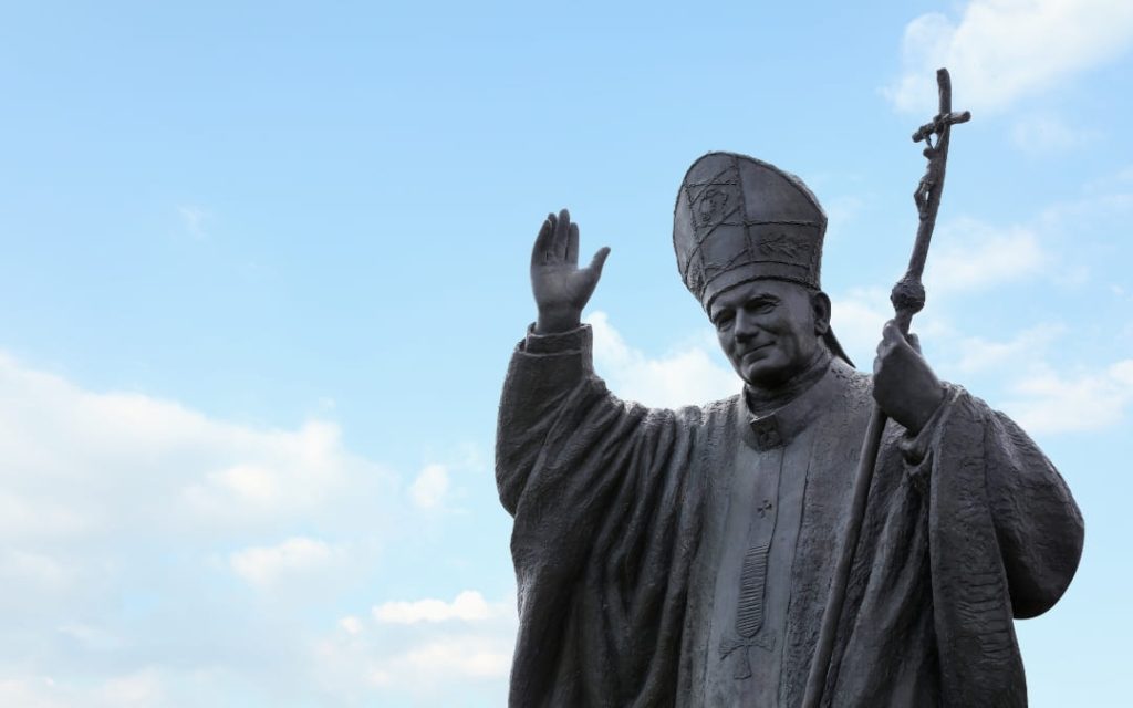 Pomnik papieża w stroju pontyfikalnym z pastorałem na tle błękitnego nieba