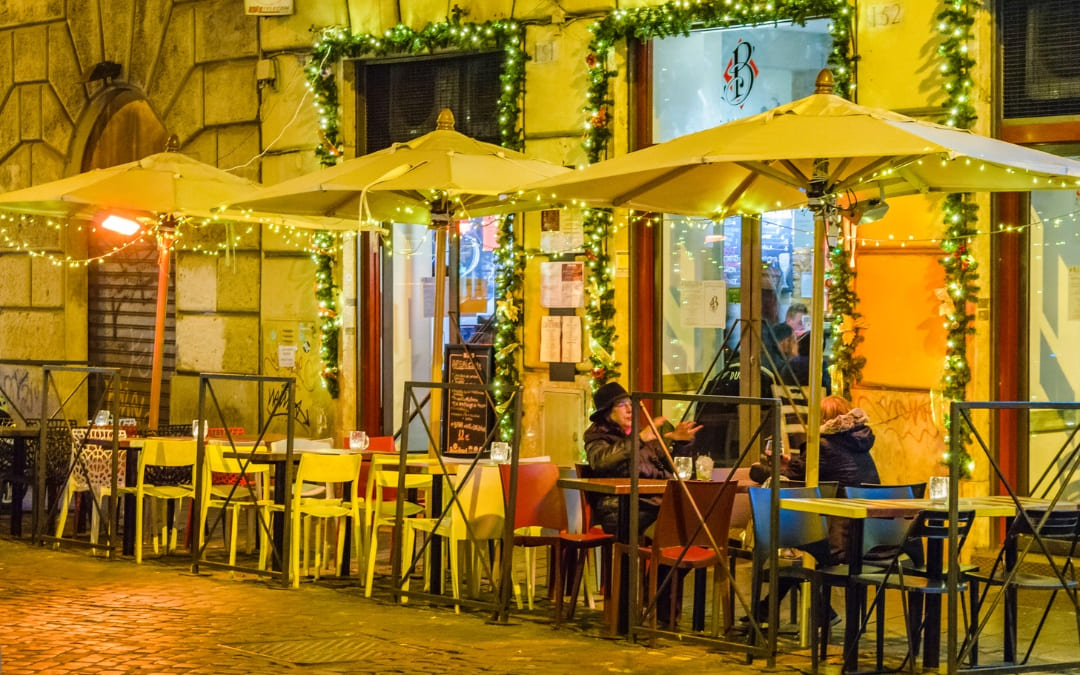 Przytulny ogródek restauracyjny przy brukowanej ulicy w Rzymie udekorowany świątecznymi lampkami w ciepły wieczór