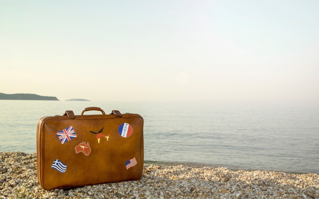 Retro walizka z naklejkami z różnych stron świata stojąca na kamienistej plaży.