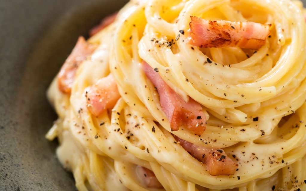 Spaghetti carbonara z boczkiem i czarnym pieprzem na ciemnym talerzu