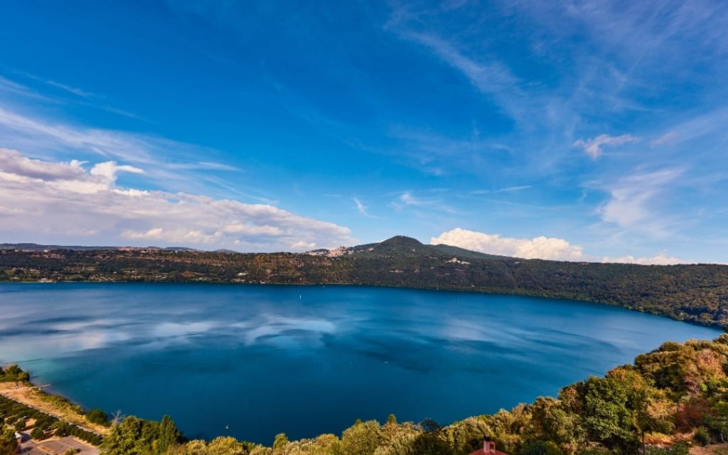 Szeroka panorama błękitnego jeziora Albano w Castel Gandolfo otoczonego zielonymi wzgórzami pod jasnym niebem