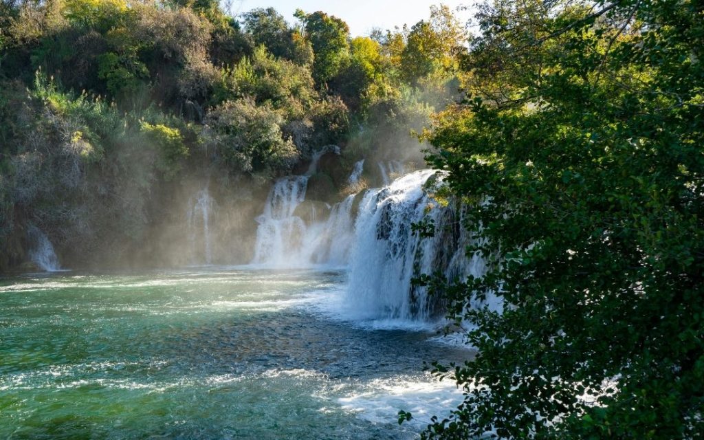 Szeroki wodospad wpadający do zielonego jeziora otoczonego gęstym lasem w Parku Narodowym Krka w Chorwacji.