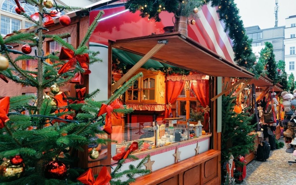 Tradycyjna drewniana budka jarmarku bożonarodzeniowego bogato udekorowana girlandami, czerwonymi kokardami i bombkami.