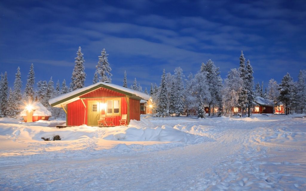 Tradycyjny czerwony drewniany domek w ośnieżonej Laponii otoczony lasem iglastym po zmroku.