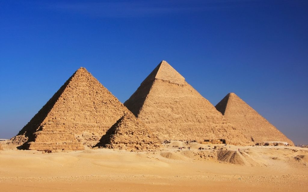 Trzy wielkie piramidy w Gizie na tle bezchmurnego, niebieskiego nieba na egipskiej pustyni.