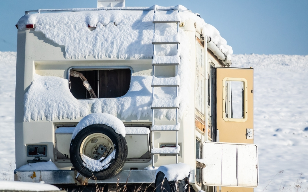 Tył białego kampera częściowo zasypanego śniegiem, zaparkowanego na ośnieżonym terenie.