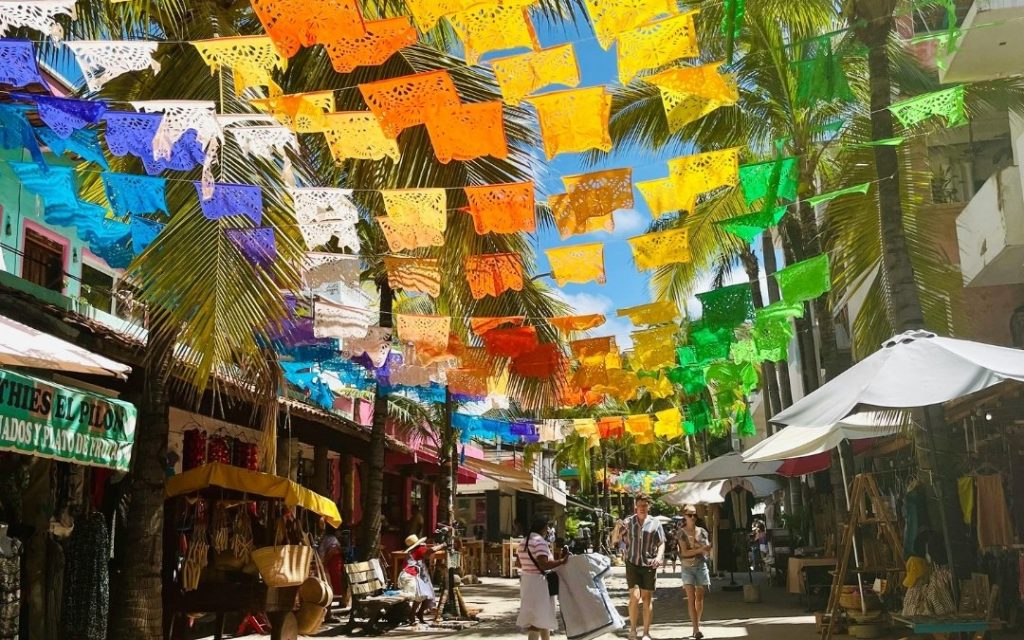 Ulica w meksykańskim miasteczku ozdobiona kolorowymi girlandami „papel picado” w słoneczny dzień.