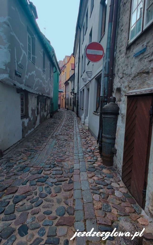 Urokliwa, wąska i brukowana uliczka ryskiej starówki z kolorowymi fasadami kamienic