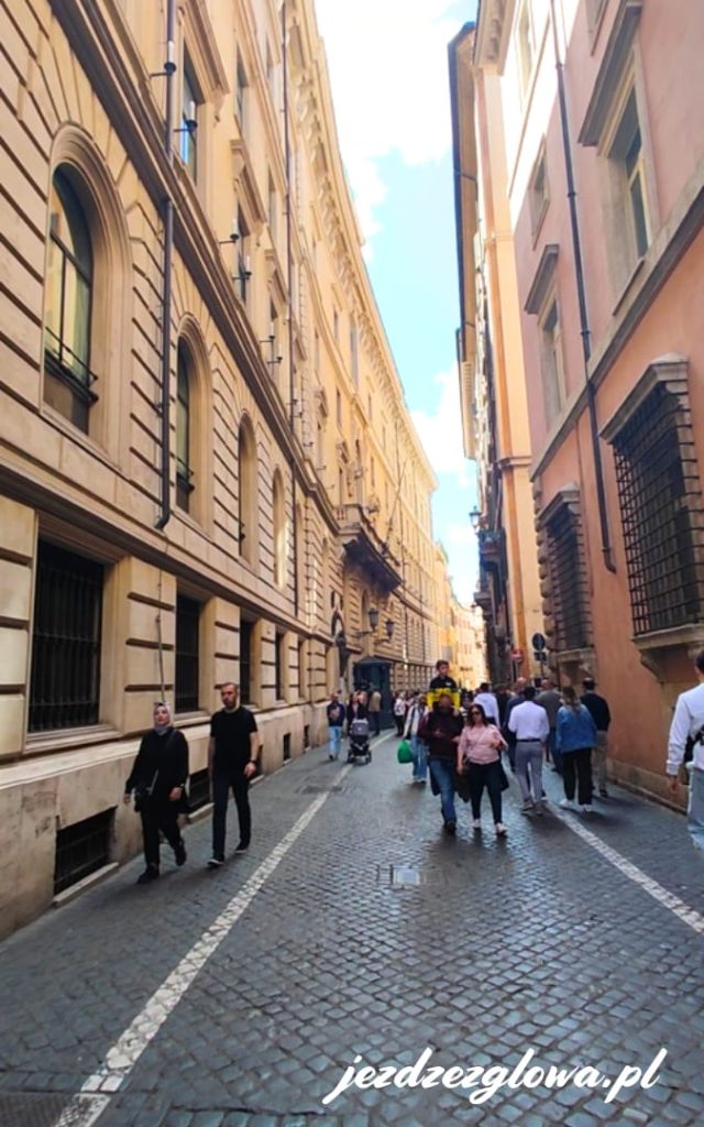 Wąska brukowana uliczka w centrum Rzymu z wysokimi kamienicami i spacerowiczami