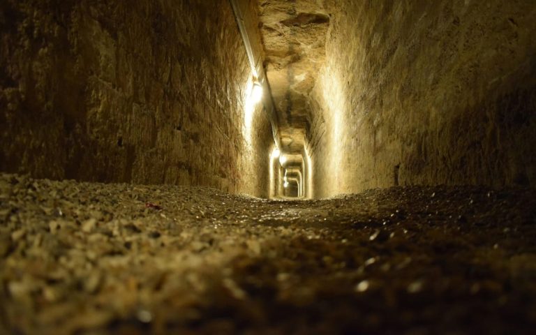 Wąski wykuty w skale podziemny korytarz oświetlony punktowym światłem wzdłuż sufitu