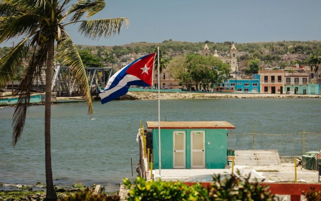Widok na zatokę na Kubie z tradycyjną zabudową i flagą kubańską powiewającą na wietrze.
