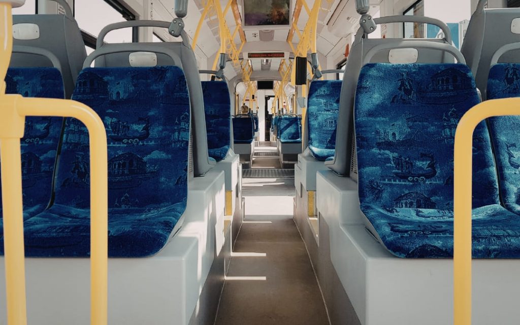 Widok wzdłuż pustej nawy autobusu z niebiesko-wzorzystymi siedzeniami i żółtymi poręczami