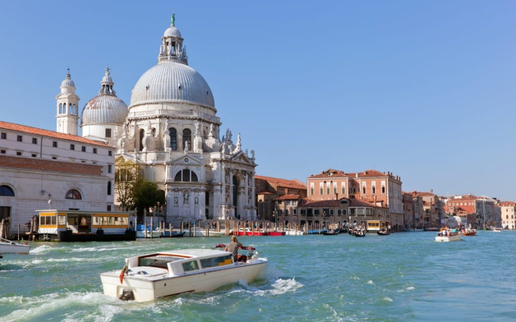 Widok z wody na Bazylikę Santa Maria della Salute z białą kopułą i barokową, bogato zdobioną fasadą