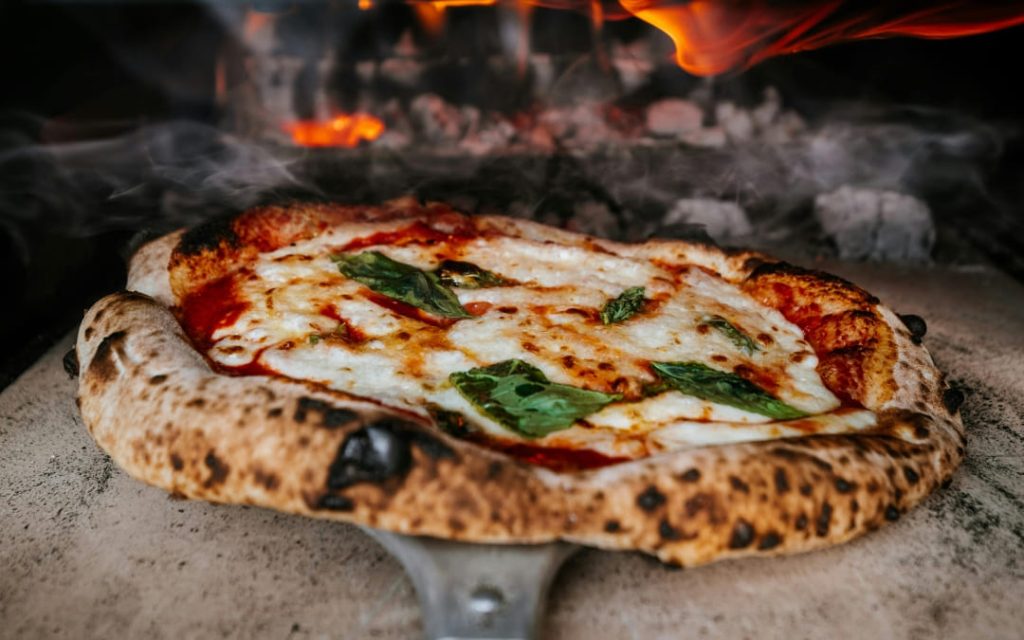 Włoska pizza wyciągana z pieca z mozzarellą i świeżą bazylią 