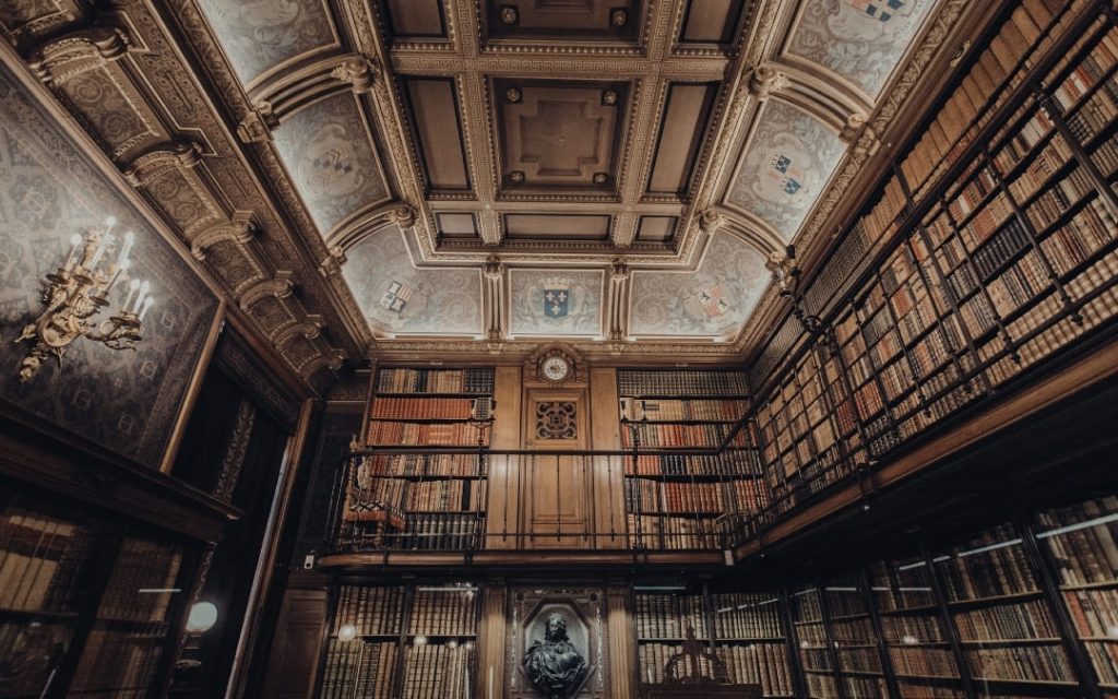 Wnętrze zabytkowej biblioteki z dwupoziomowymi regałami pełnymi ksiąg i zdobionym stropem