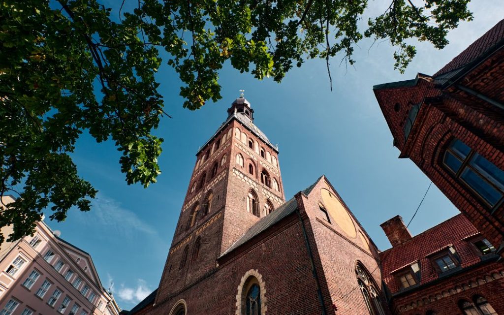 Wysoka ceglana wieża kościelna widziana z dołu na tle nieba i drzew.