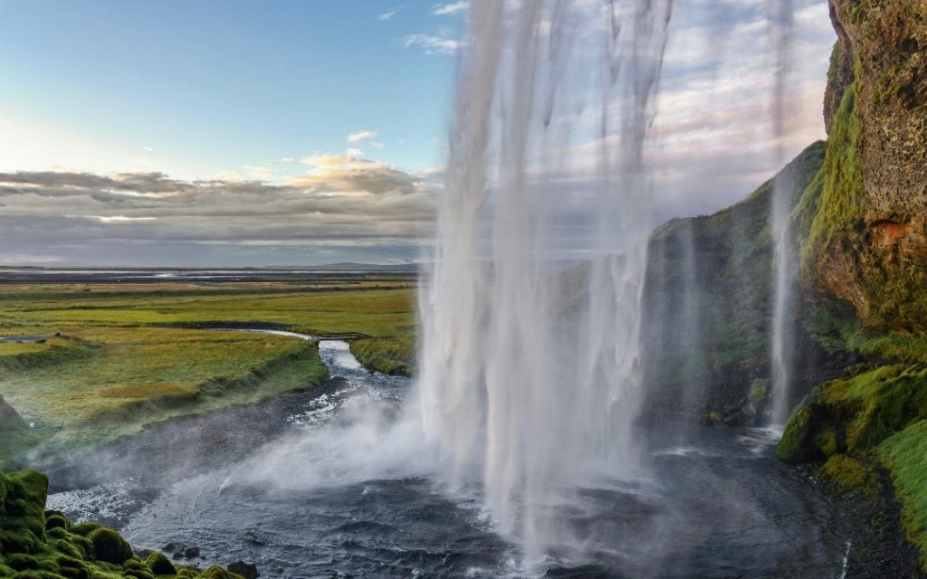 Wysoki wodospad Seljalandsfoss na Islandii opadający z porośniętego mchem urwiska pod zachmurzonym niebem.