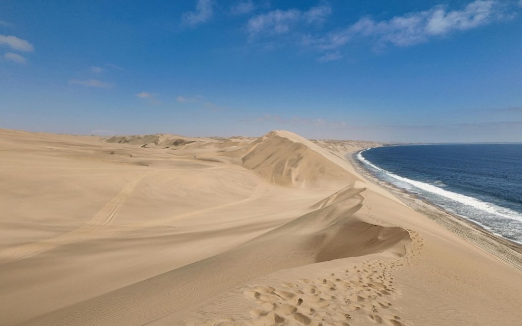 Wysokie piaszczyste wydmy pustyni Namib stykające się bezpośrednio z falami oceanu.
