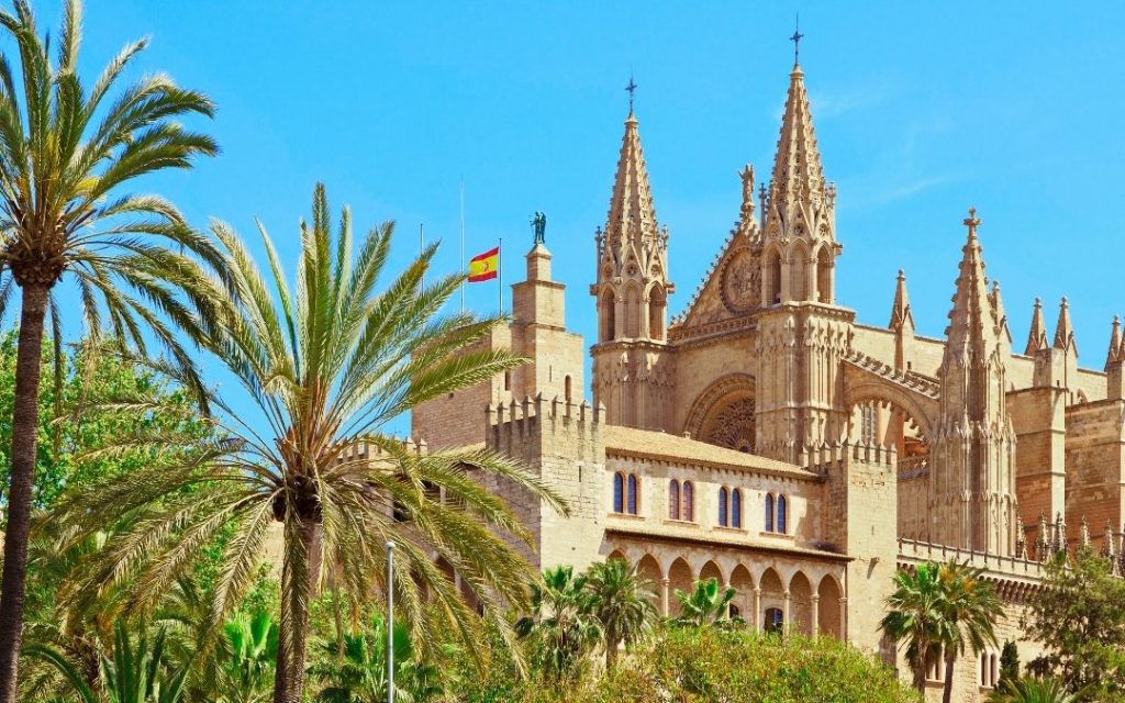 Zabytkowa katedra La Seu w Palmie na Majorce otoczona palmami pod błękitnym niebem.
